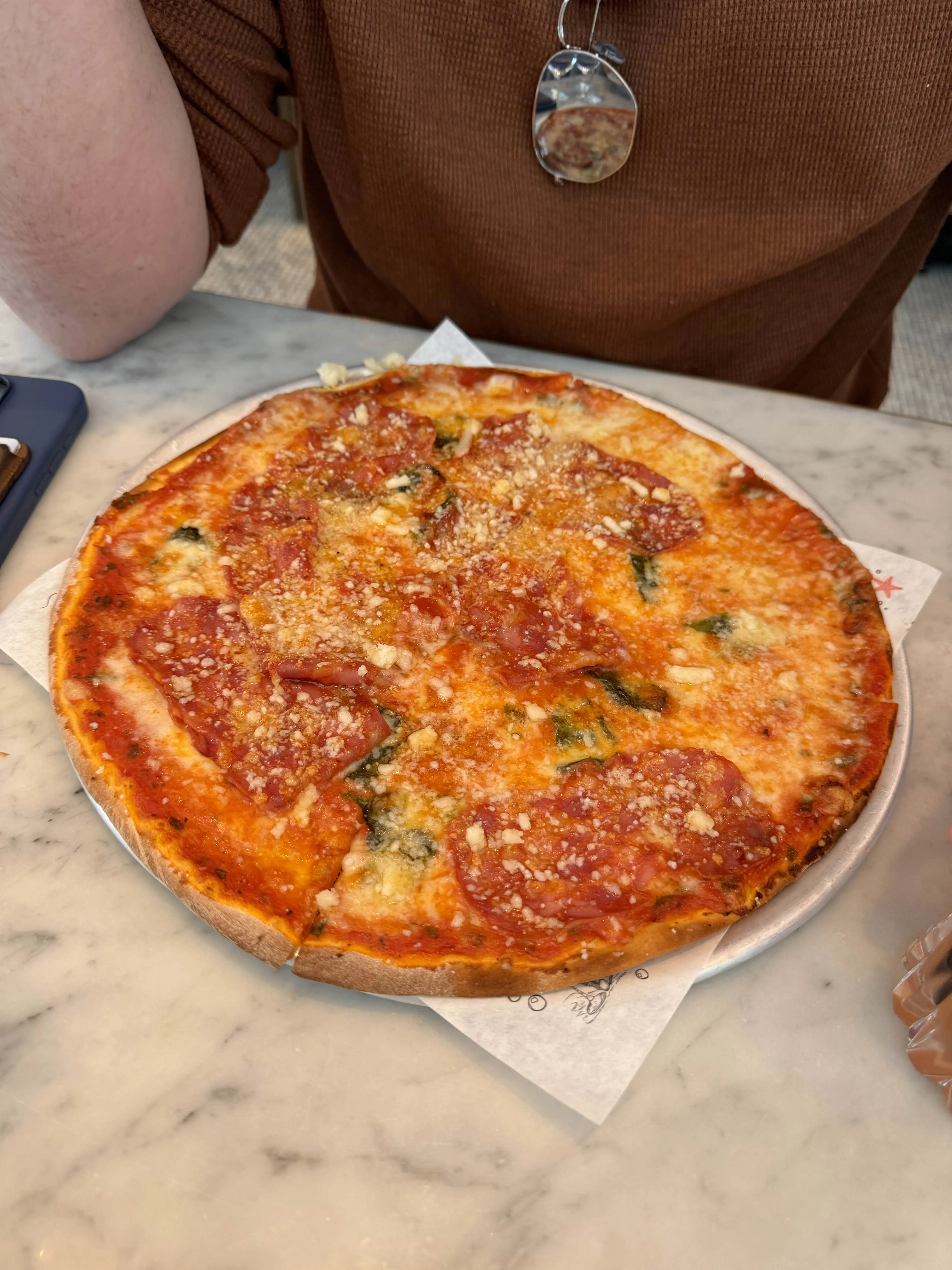 A thin-crust pizza dotted with salami, viewed from above on the same marble table.