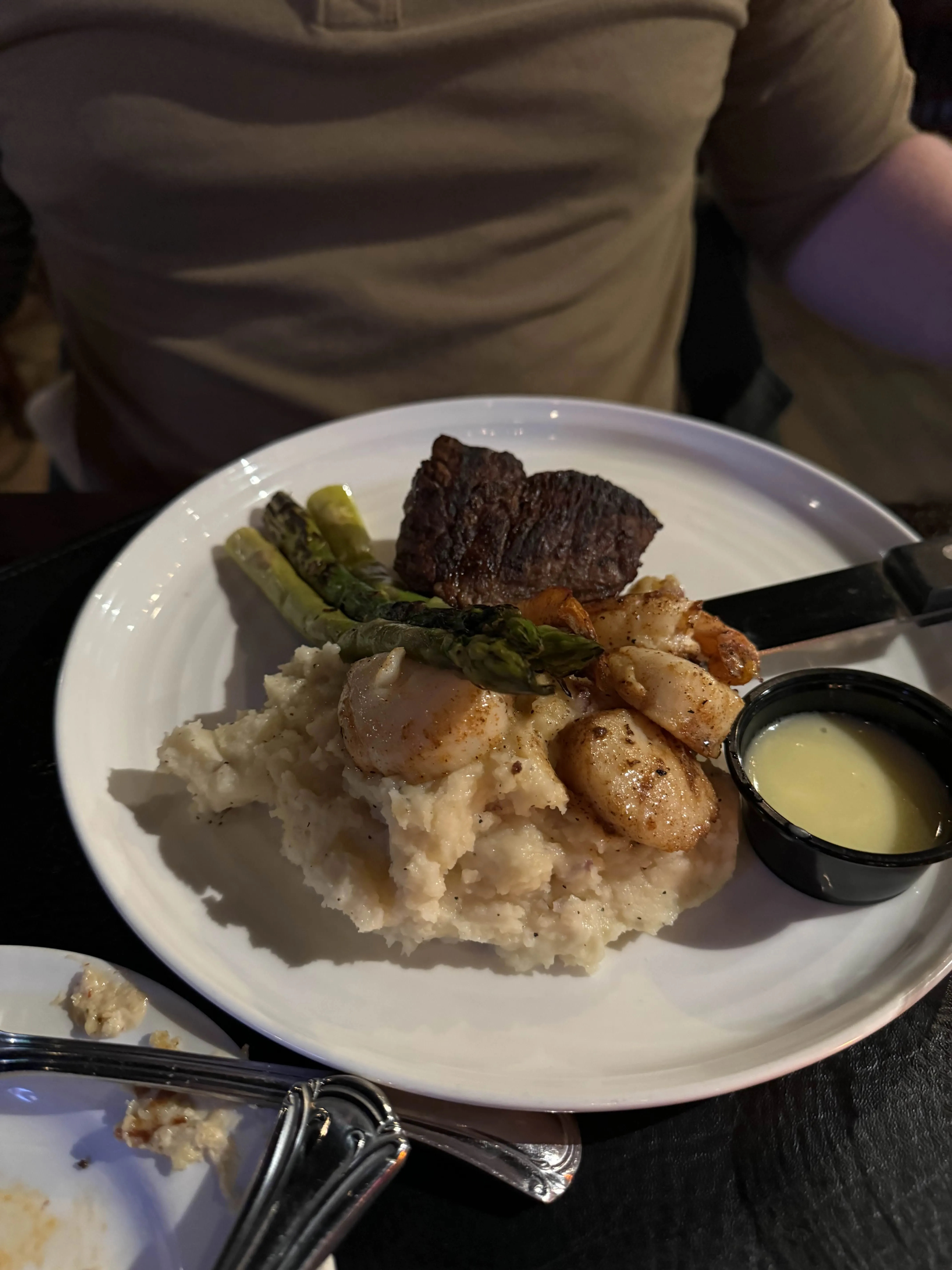 A small steak, a row of pan-seared scallops, a few spears of asparagus and a ramekin of drawn butter, all set on a mound of mashed potatoes.