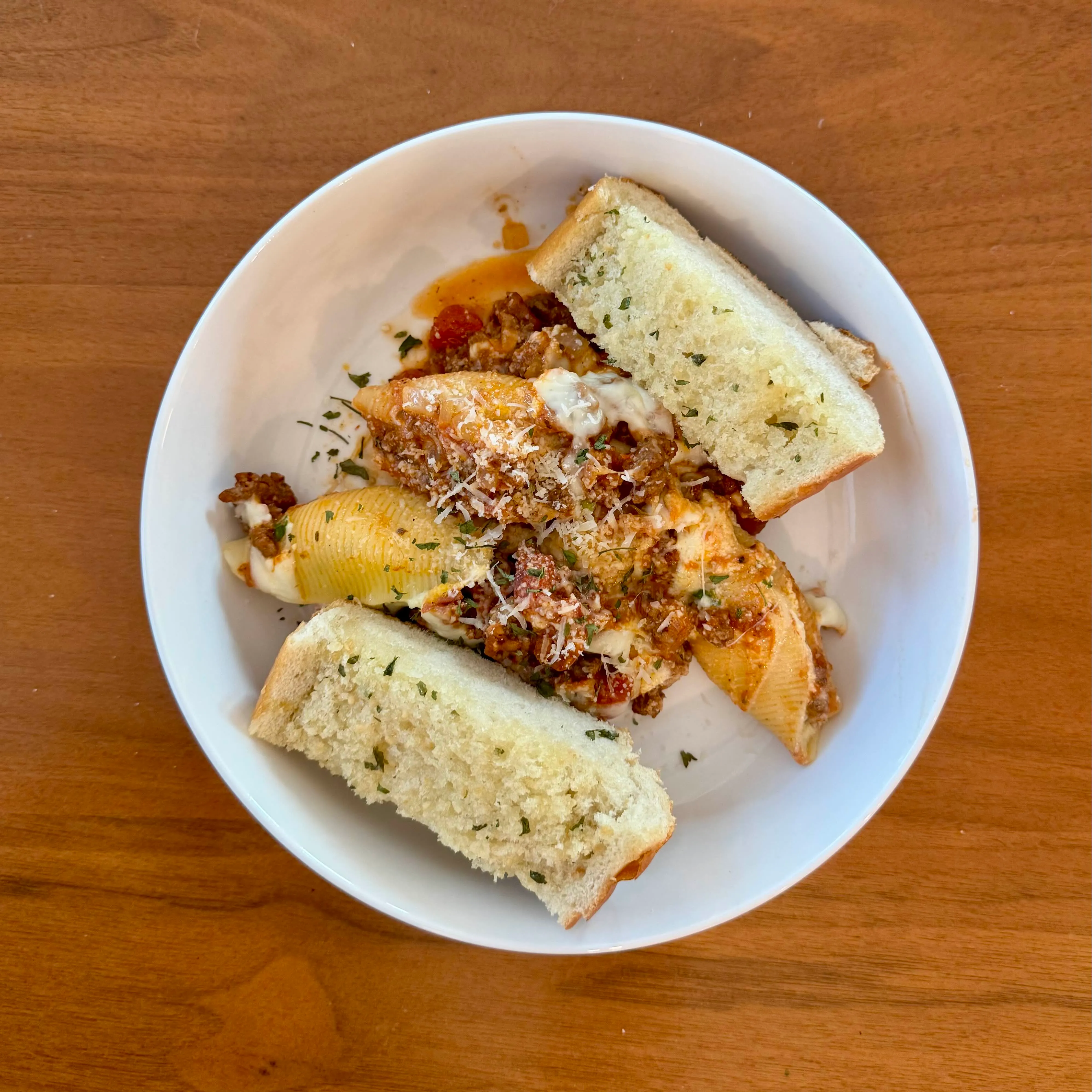 A bowl of jumbo stuffed pasta shells in red sauce with melted cheese peeking out, flanked by two thick slices of garlic bread.