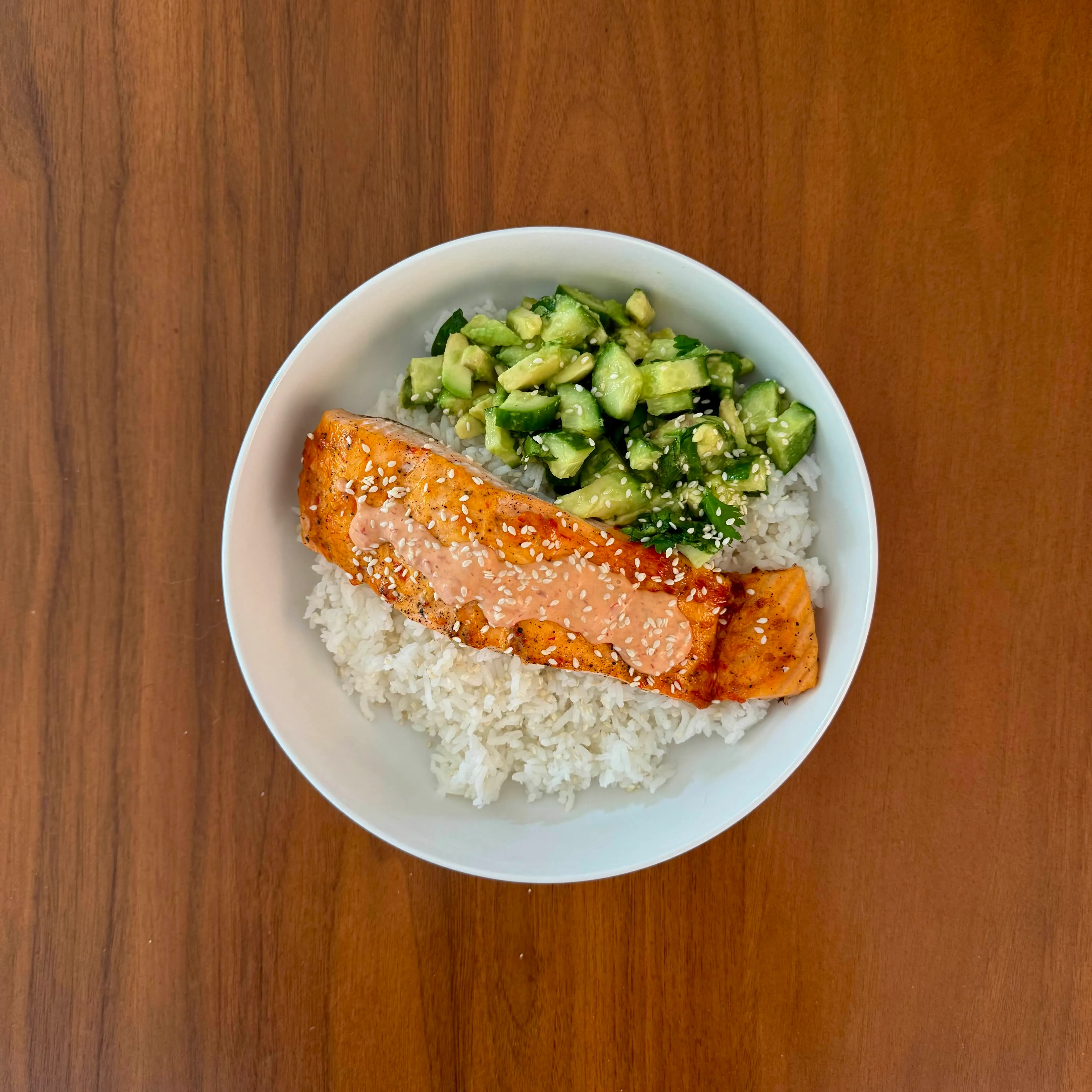 Sesame-glazed salmon on white rice beside a cucumber-avocado salad dressed with sesame.