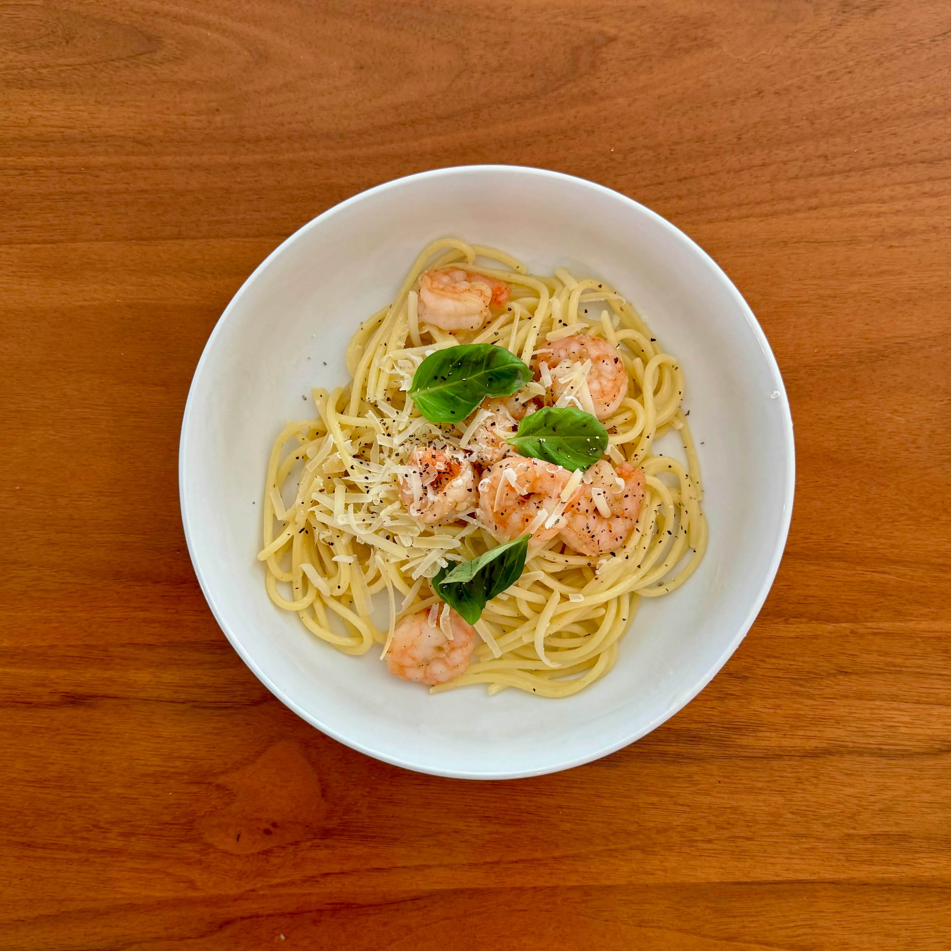 A bowl of spaghetti aglio e olio with pink shrimp, torn basil leaves, and shaved parmesan.