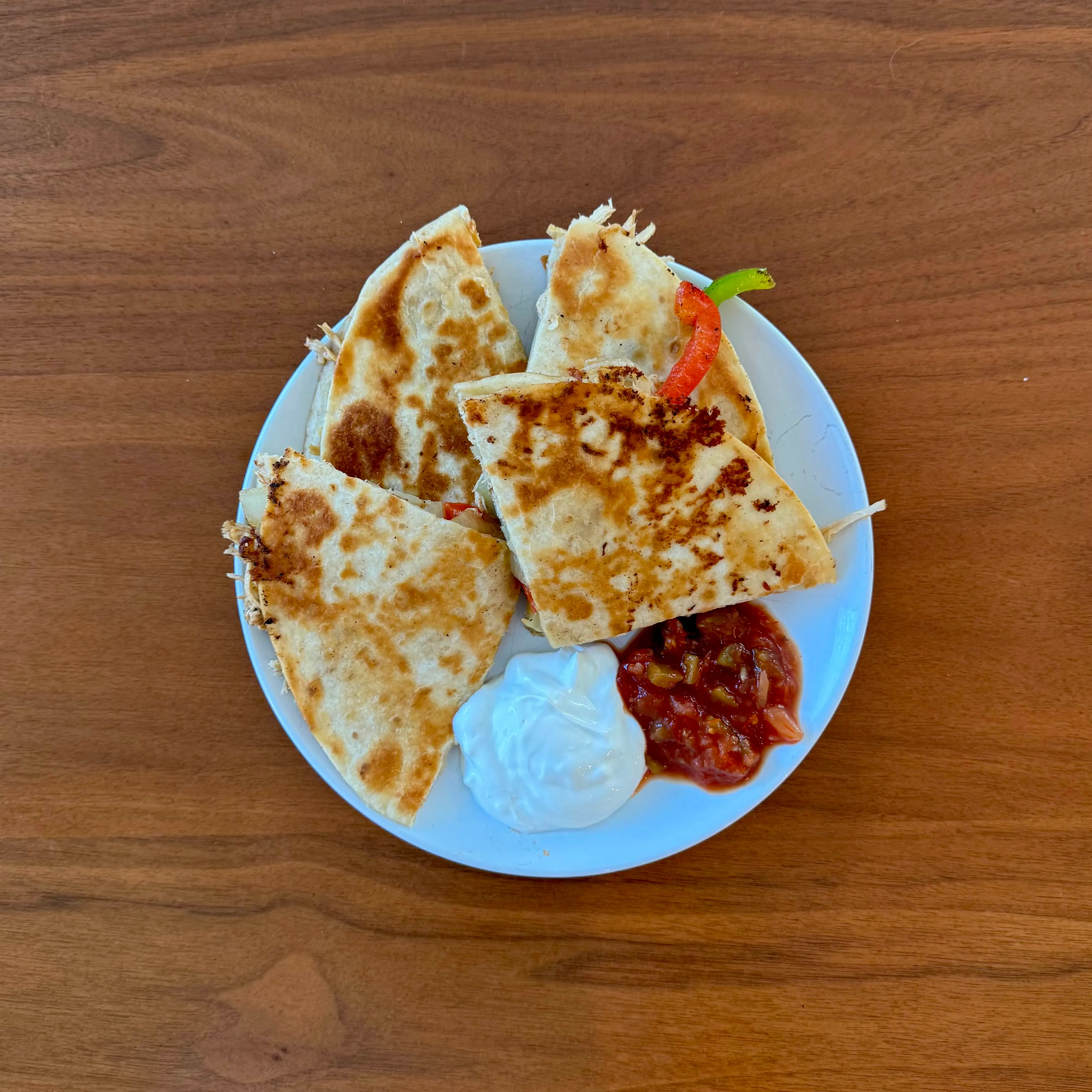 Quesadilla wedges on a white plate with small scoops of salsa and sour cream on the side.