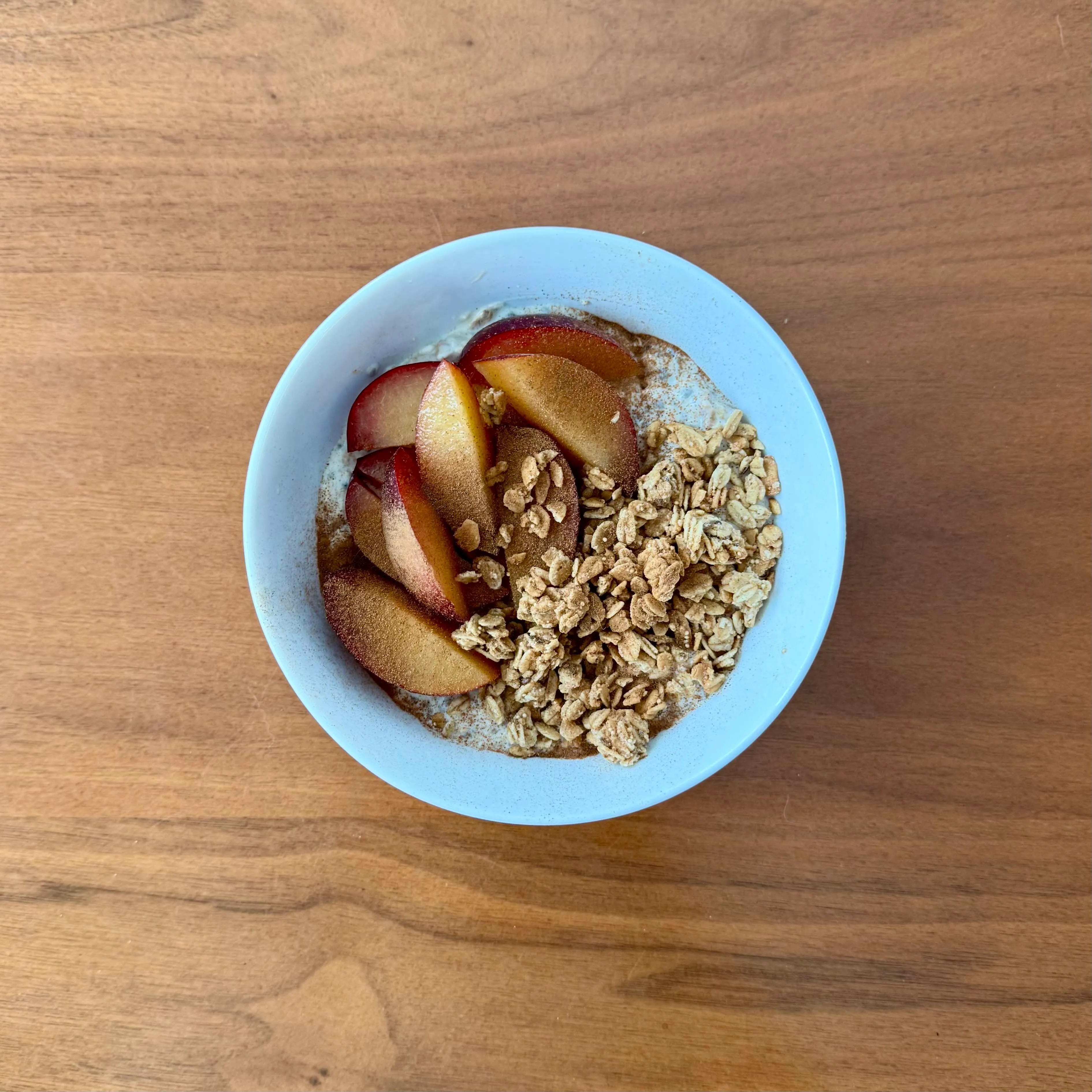 A bowl of oatmeal or yogurt topped with sliced red-skinned plums and a mound of crunchy granola.