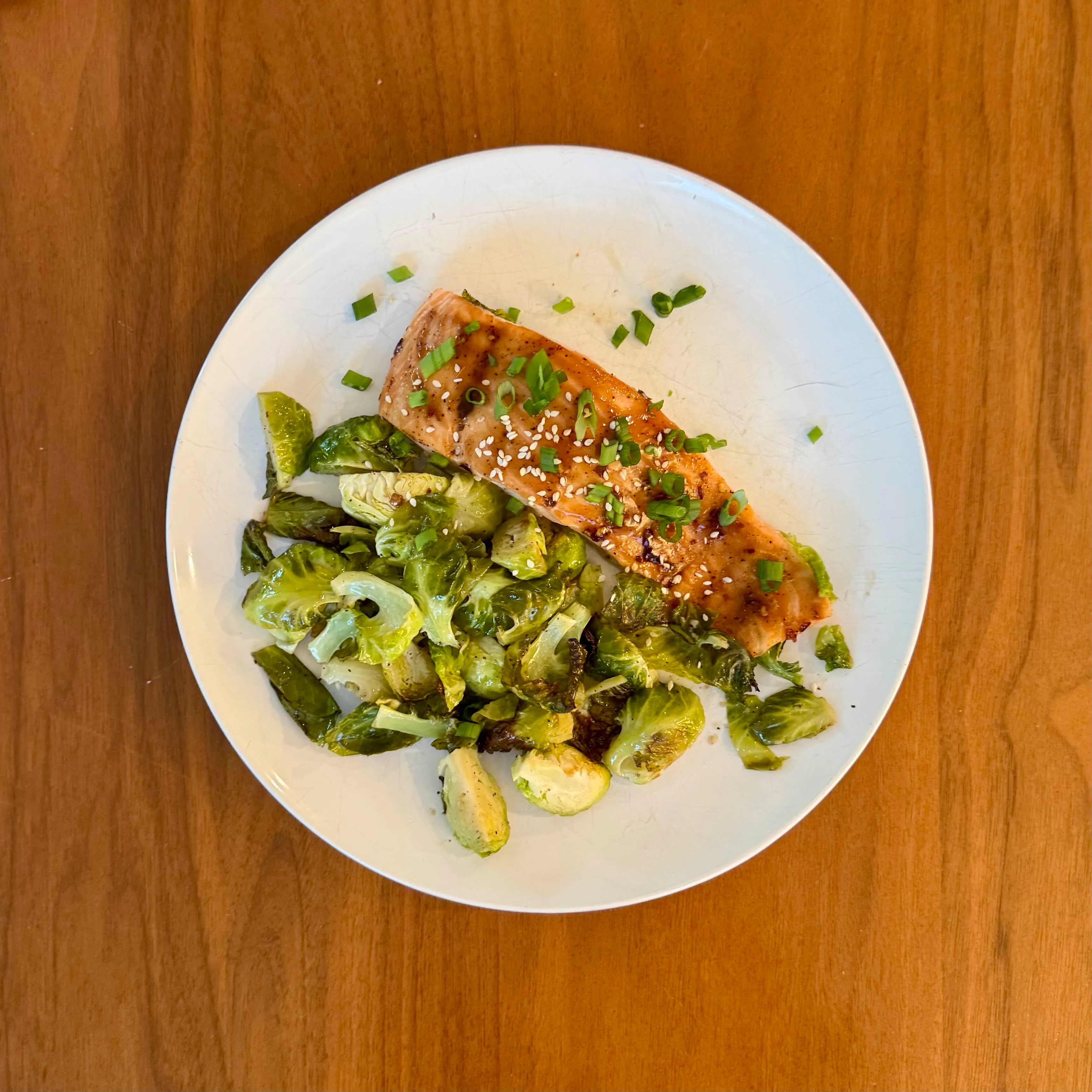 A piece of glazed teriyaki salmon with sesame and scallions beside halved roasted brussels sprouts.