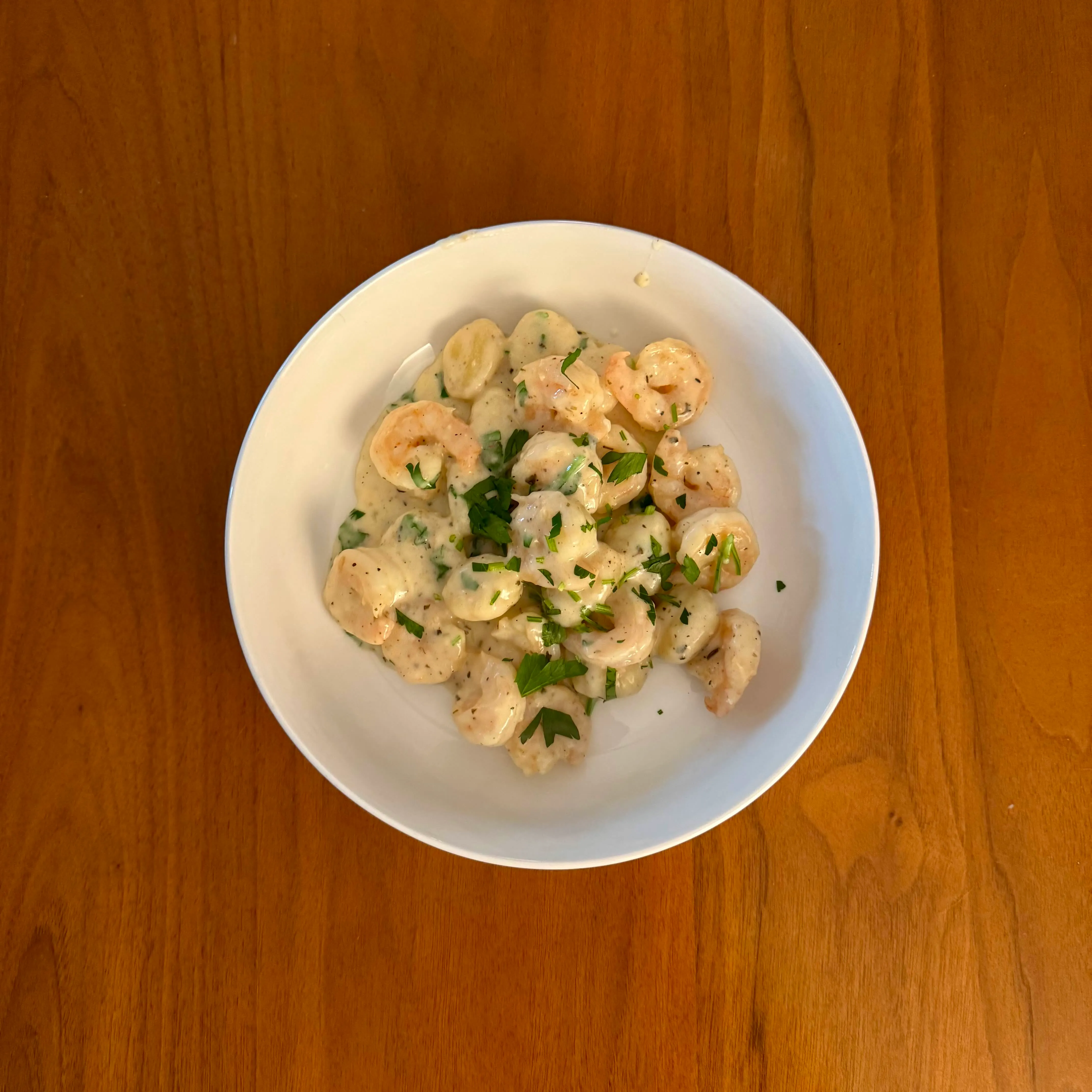 A shallow bowl of small shrimp and tiny pasta rings in a pale garlic-butter sauce, finished with chopped parsley.
