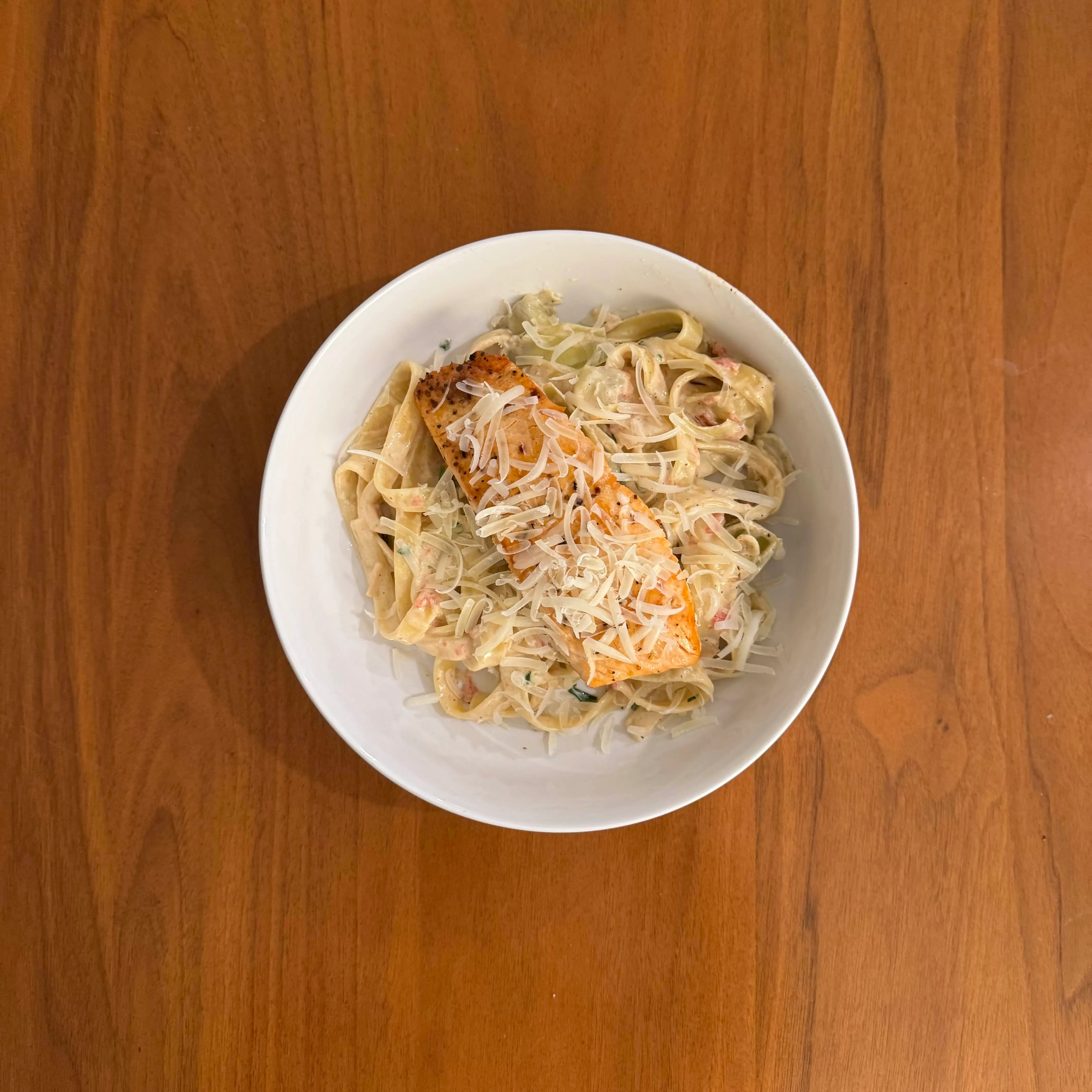 A pan-seared salmon fillet on a nest of fettuccine alfredo with shaved parmesan.