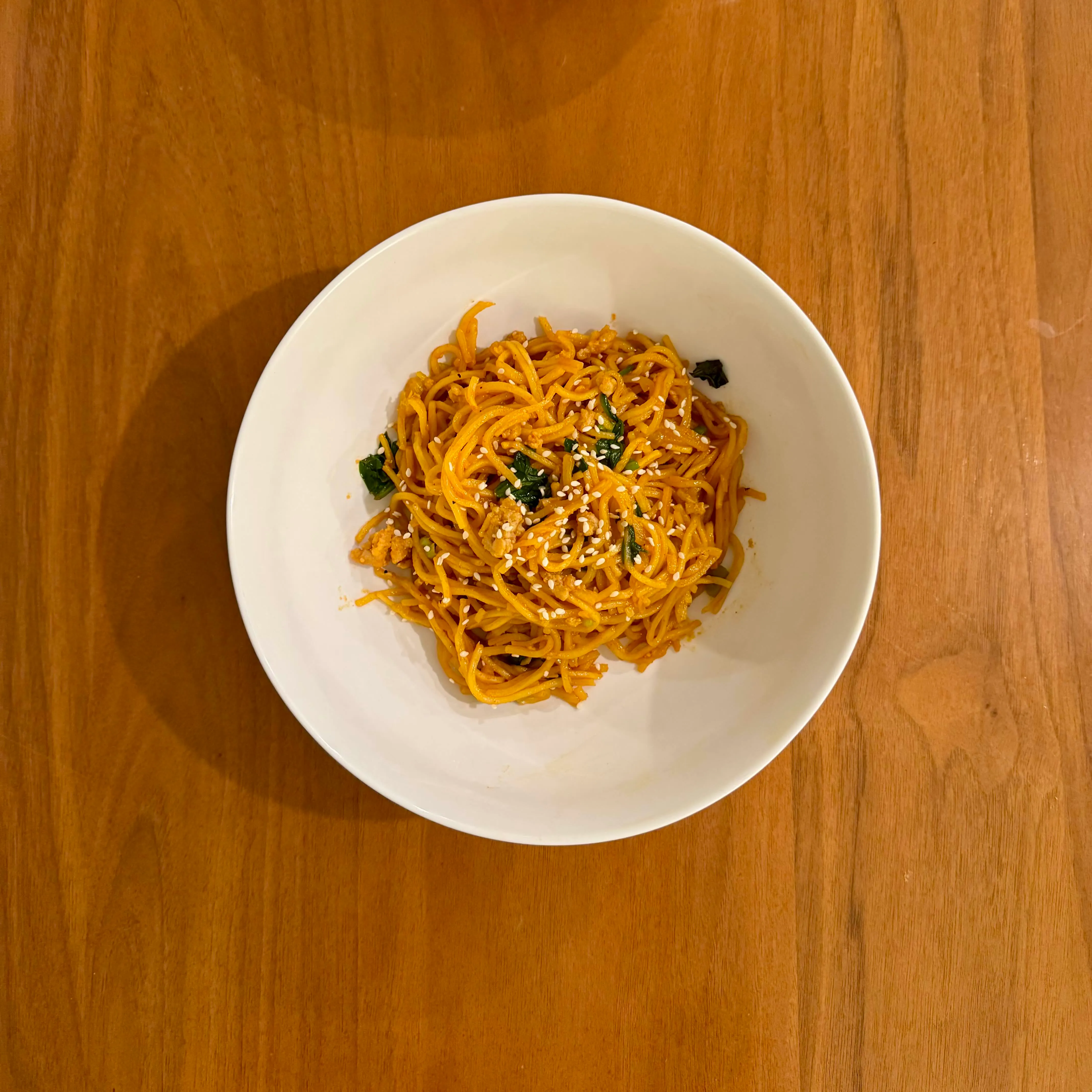 A bowl of spaghetti tossed with sesame-soy sauce and wilted spinach, sesame seeds scattered over the top.