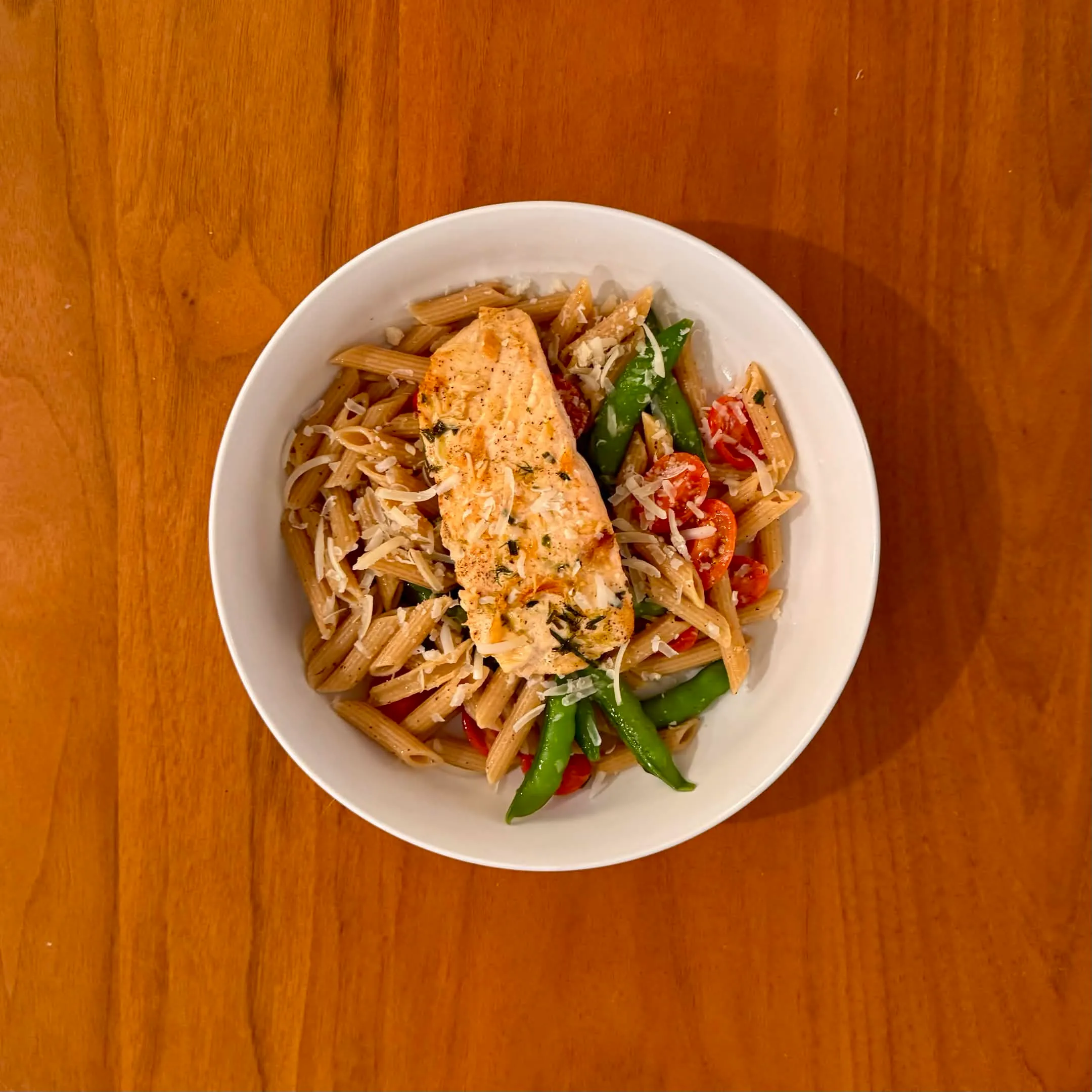 A bowl of penne with grilled chicken, halved cherry tomatoes, and cut green beans, dusted with parmesan.