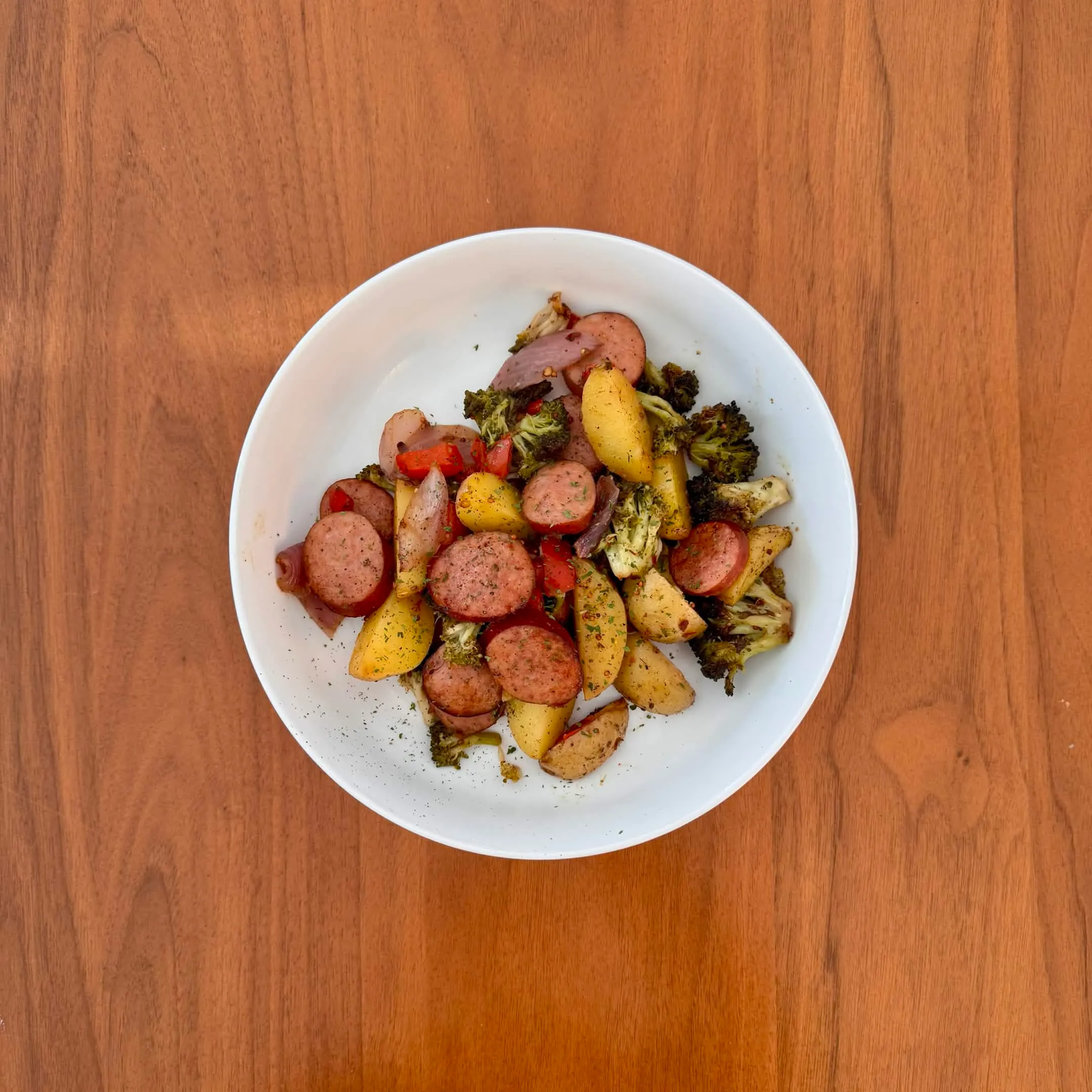 A bowl of sheet-pan smoked sausage coins with roast potato chunks, broccoli, and red peppers.
