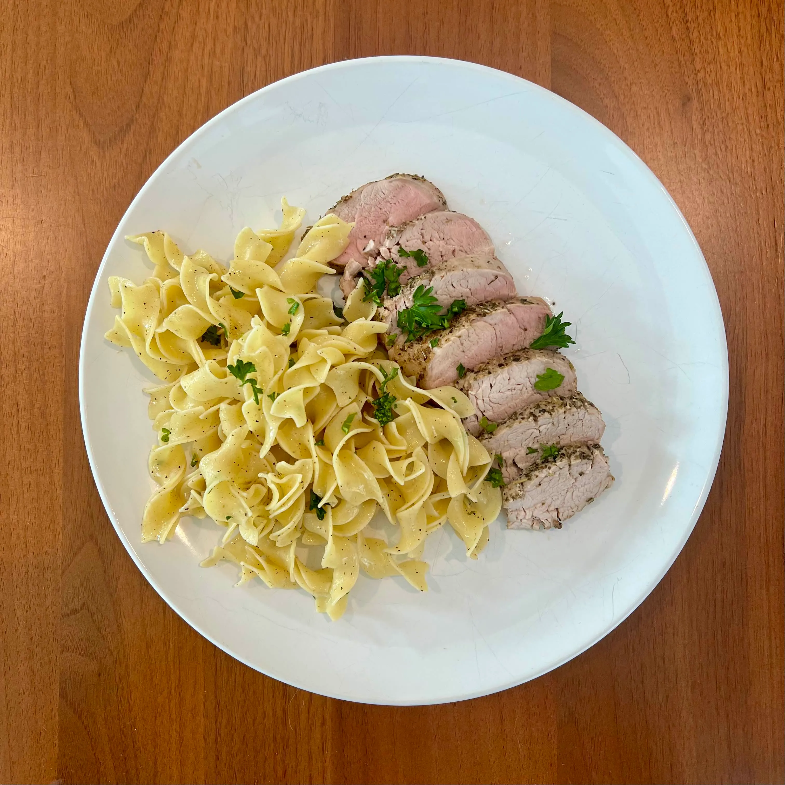 Sliced herb-crusted pork tenderloin fanned over buttered egg noodles, flecked with parsley.